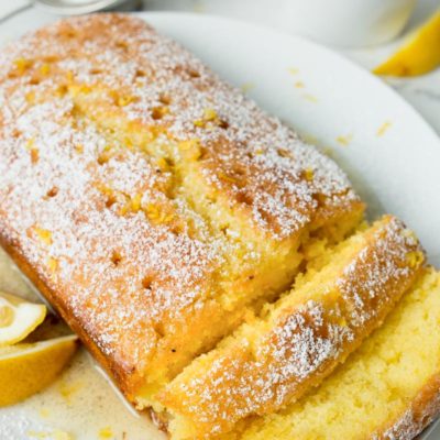 Lemon Drizzle Cake on a white plate with lemon wedges