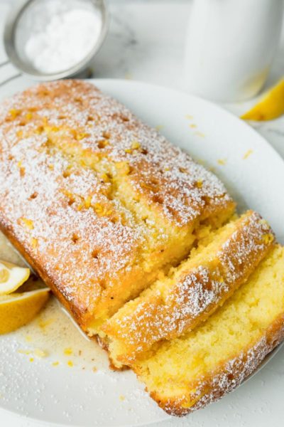 Lemon Drizzle Cake on a white plate with lemon wedges
