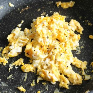 scrambled eggs being seasoned with pepper and salt
